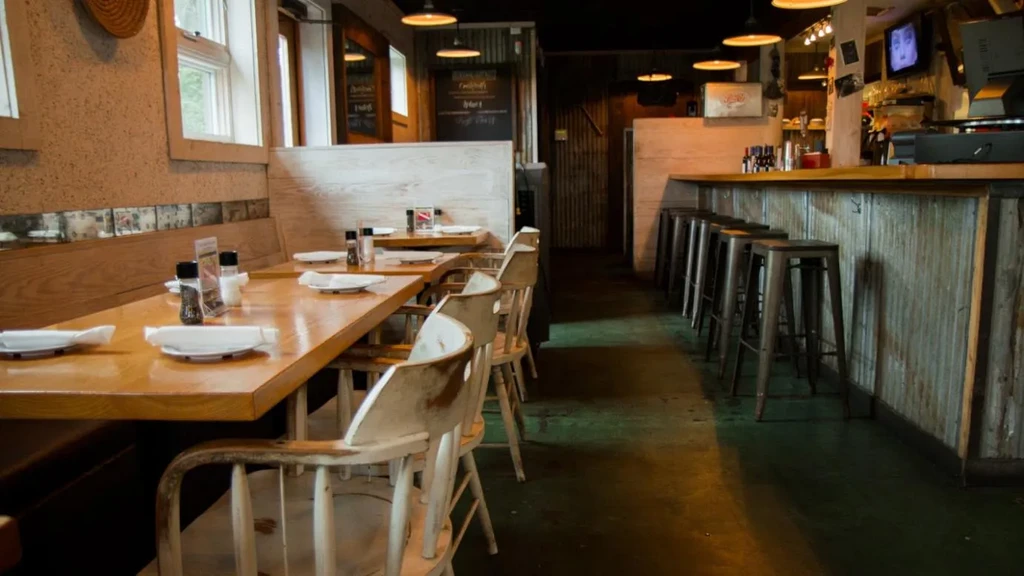 Empty casual restaurant with wooden tables, booth, and corrugated metal bar.