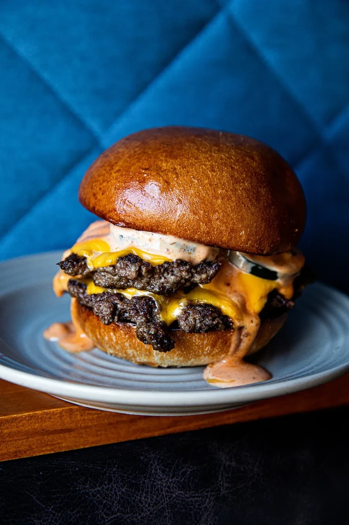 Double smash burger with melted cheese, sauce, and pickle on a blue plate.