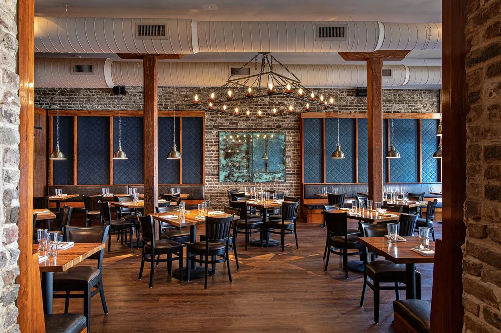 Empty rustic-industrial restaurant dining room with brick walls and wood beams.