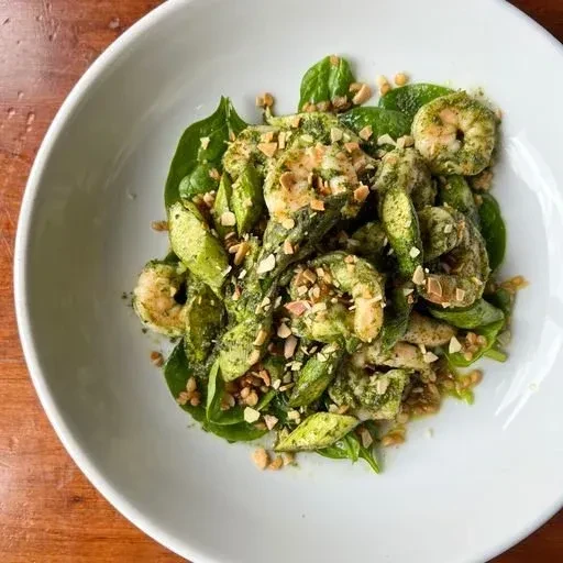 Close-up overhead of vibrant green shrimp and pesto dish with nuts.