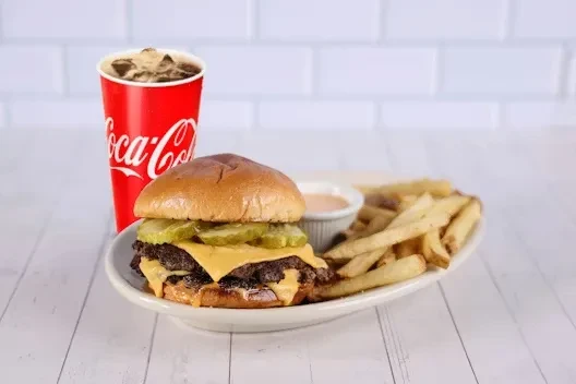 Double cheeseburger, fries, sauce, and Coca-Cola on a white table.