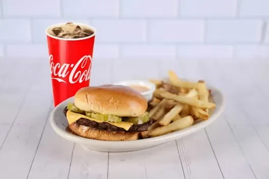 Diner cheeseburger, golden fries, dipping sauce, and Coca-Cola on a plate.