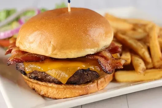 Bacon cheeseburger, golden fries, and a blurry side salad.
