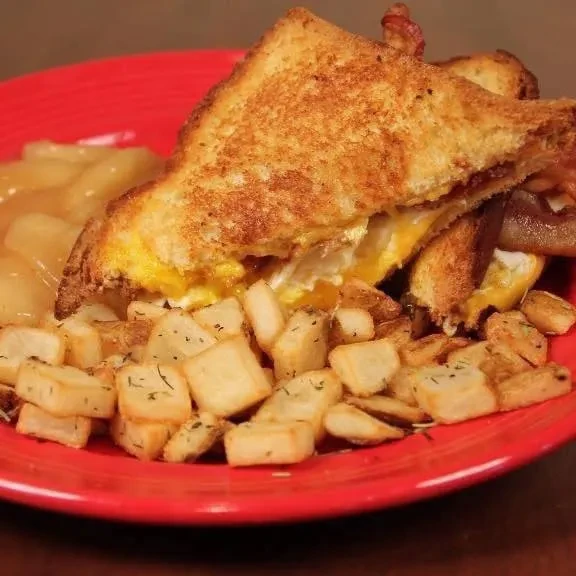 Red plate holds toasted sandwich, home fries, and stewed fruit.