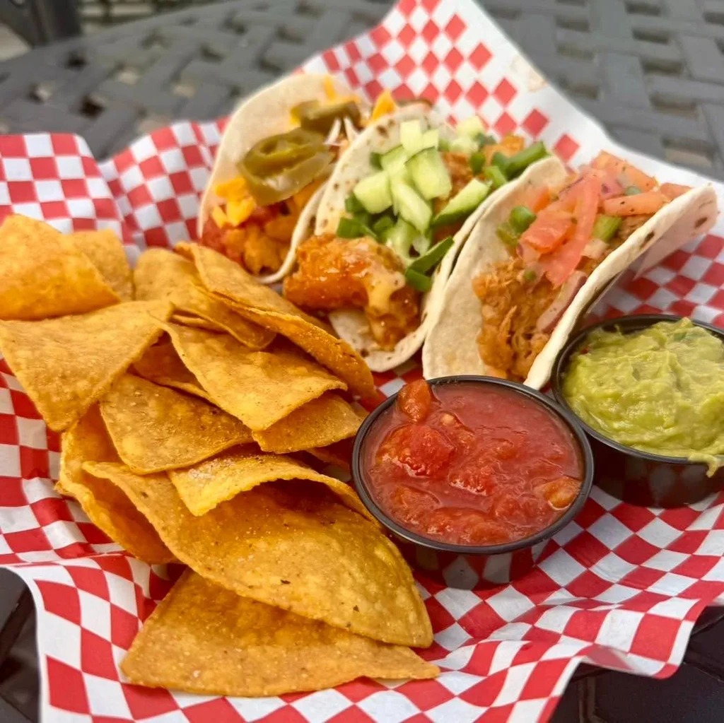 Platter with three tacos, tortilla chips, red salsa, and guacamole.