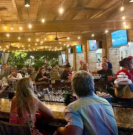 Busy evening restaurant patio with string lights, patrons, and nature scenes.