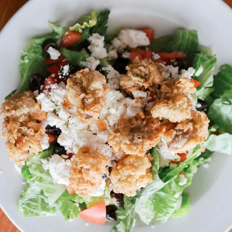Salad with lettuce, feta, tomatoes, olives, and fried golden-brown pieces.