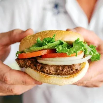 Hands hold a hamburger with beef patty, lettuce, tomato, onion.