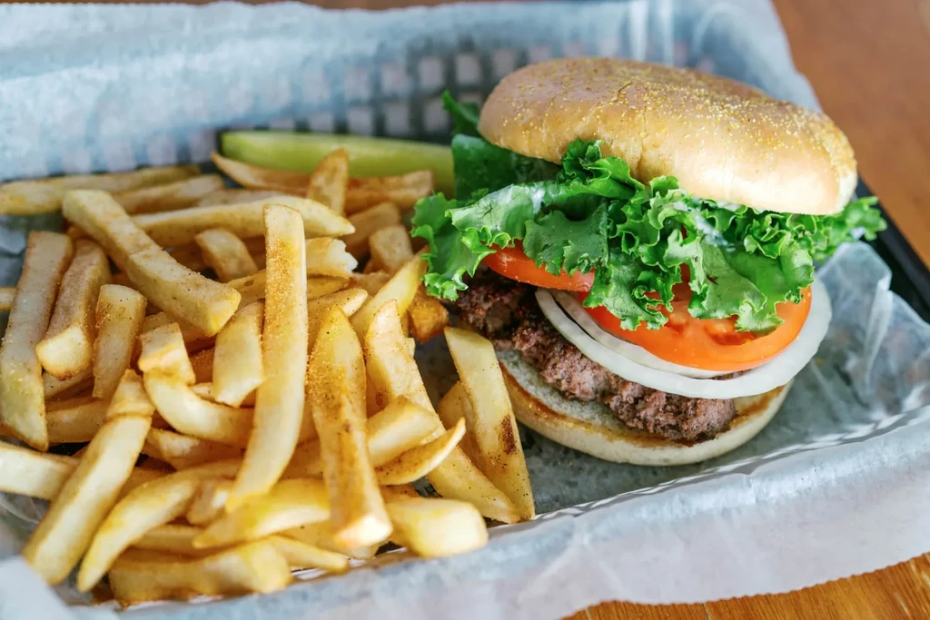 A classic hamburger, spiced fries, and pickle in a black basket.