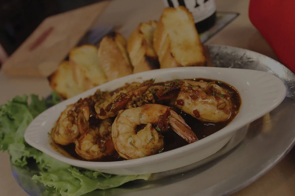 Shrimp in dark sauce, garnished with herbs, chili, and blurred bread.