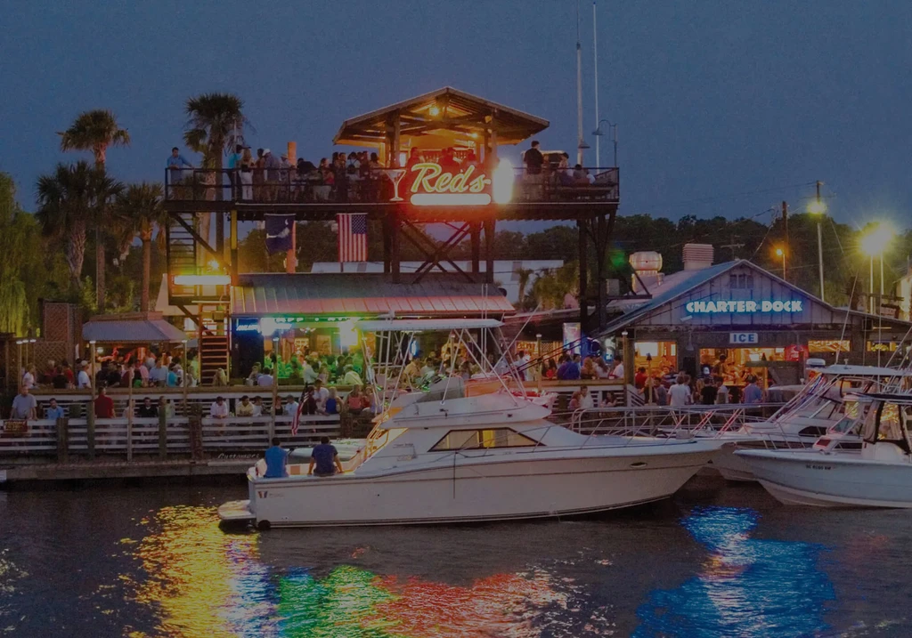 Bustling Red's waterfront restaurant at night with boats and colorful reflections.