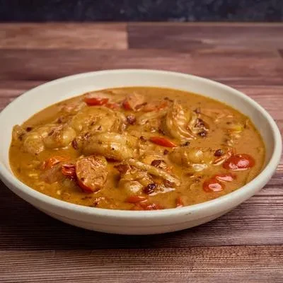 Reddish-orange shrimp and tomato curry in a white bowl on wood.