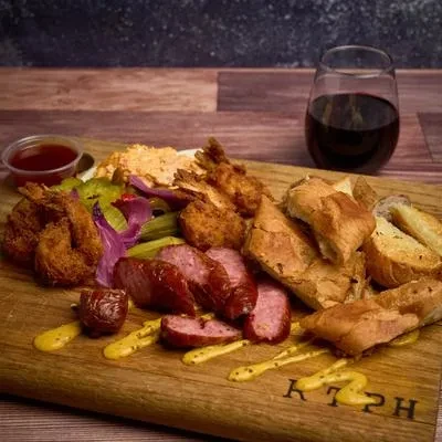 Rustic wooden board with fried shrimp, sausage, bread, vegetables, and wine.