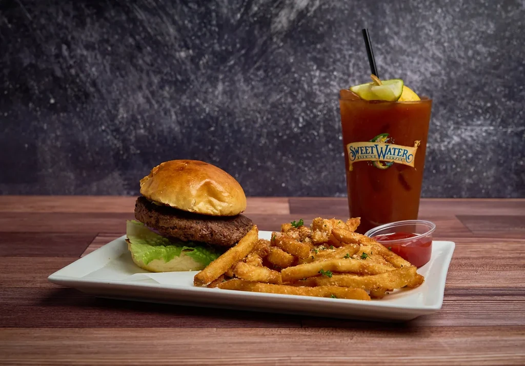 Burger, parmesan fries, and SweetWater drink on a wooden table.
