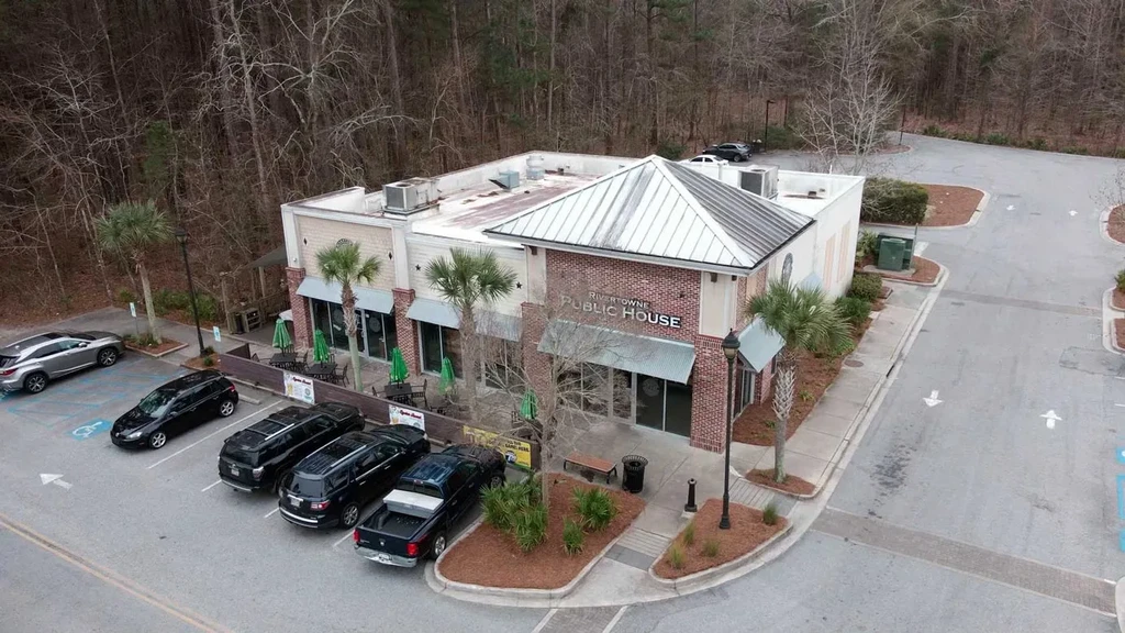 Aerial view of Rivertowne Public House, patio, parking, and bare forest.