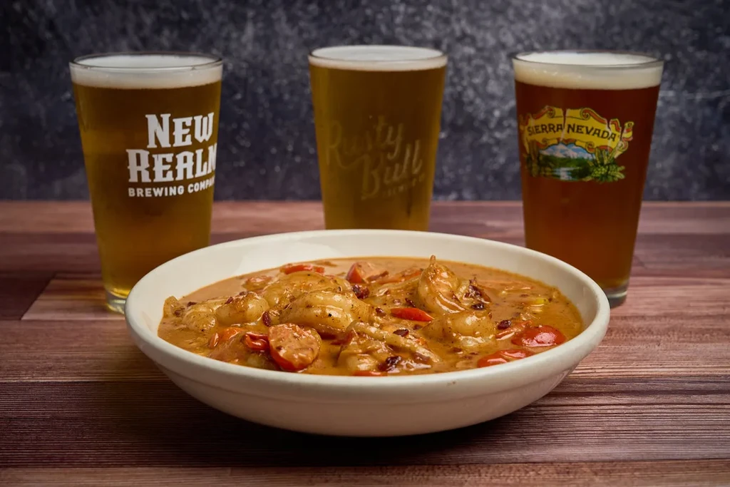 Stew with shrimp and sausage, three beers on a wooden table.