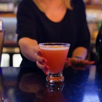 Close-up of a vibrant reddish-pink cocktail held by hand with red nails.