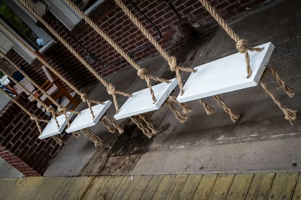 Five white wooden boards suspended diagonally by ropes against a brick wall.