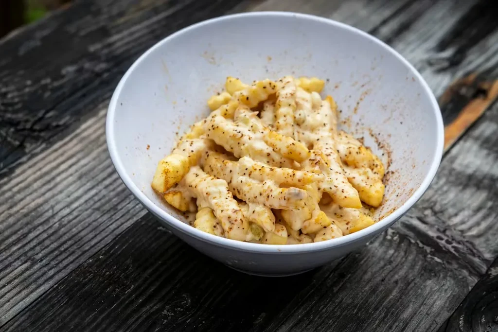 White bowl of crinkle-cut fries with melted cheese on rustic wood.