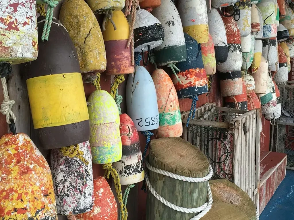 Weathered, colorful lobster buoys and traps hang against rustic planks.