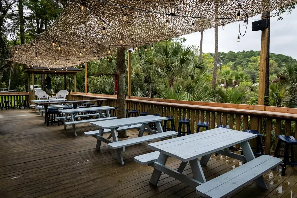 Tropical outdoor restaurant deck with blue picnic tables and bar stools.