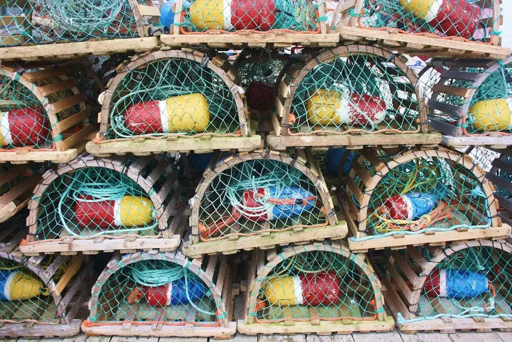 Weathered wooden lobster traps stacked with vibrant buoys and ropes.