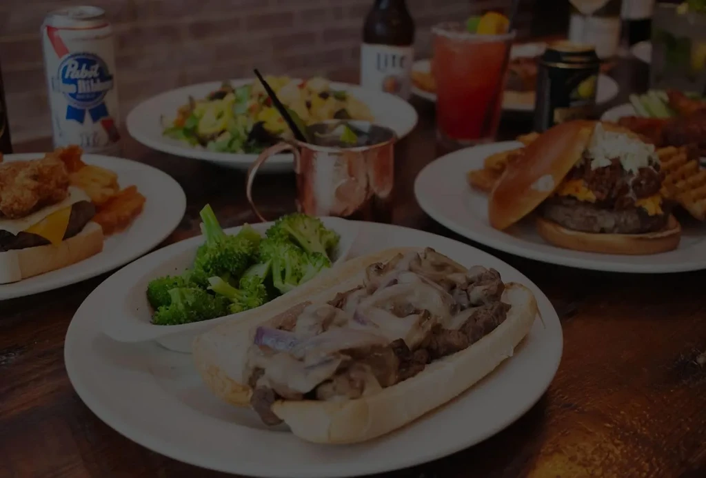 Spread of sandwiches, burgers, fries, broccoli, beer, and cocktails.