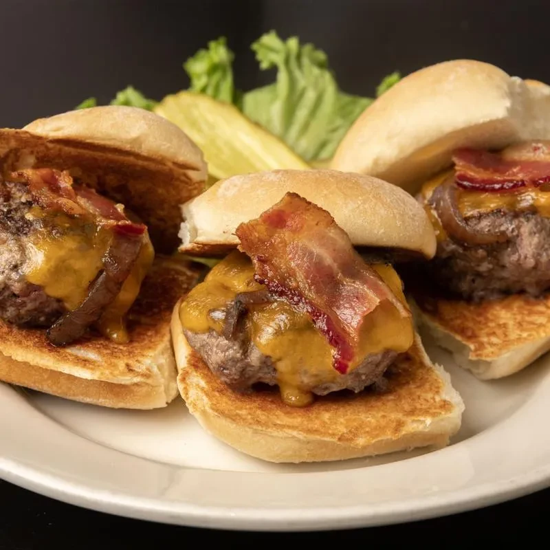 Three beef sliders with melted cheese, bacon, and onions.