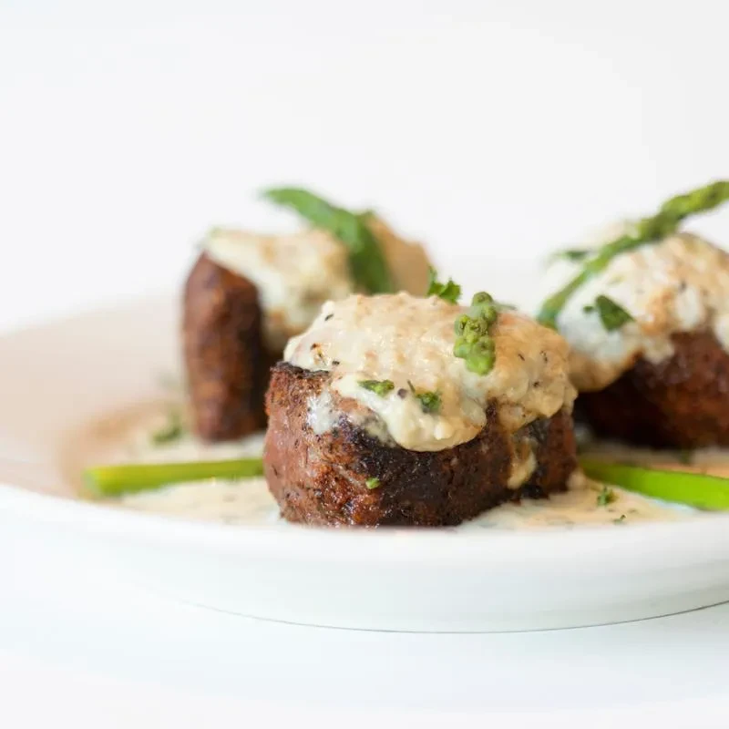 Seared meat medallions with creamy sauce and green garnish on white plate.