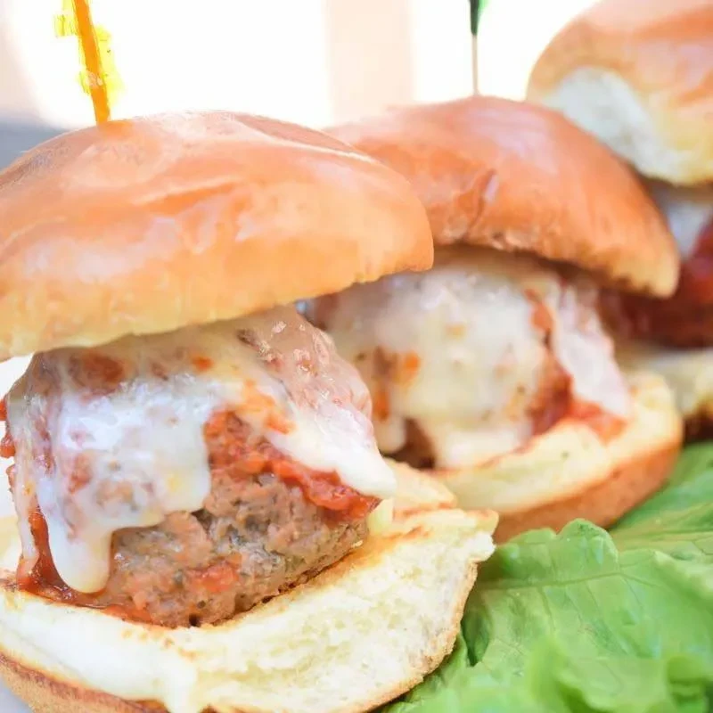 Three meatball sliders topped with melted cheese, marinara, and lettuce.