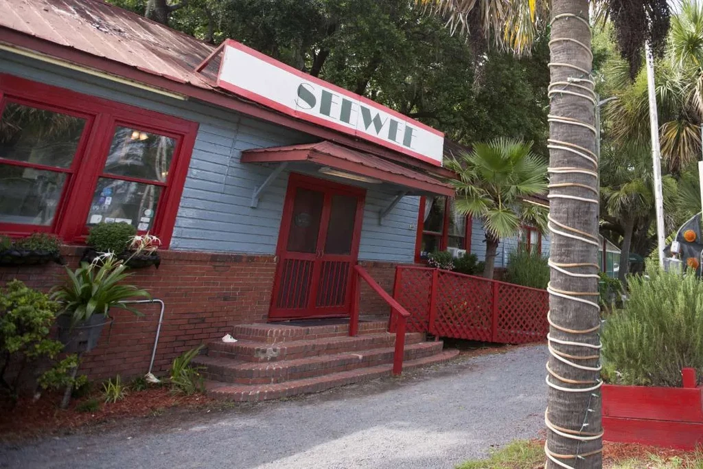 Light blue Seewee restaurant with red roof, brick, and palm trees.