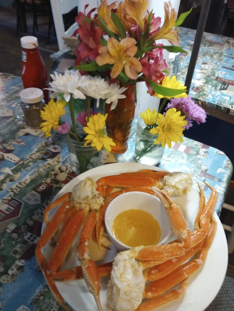 Close-up of cooked snow crab legs, butter, and flowers on a patterned table.