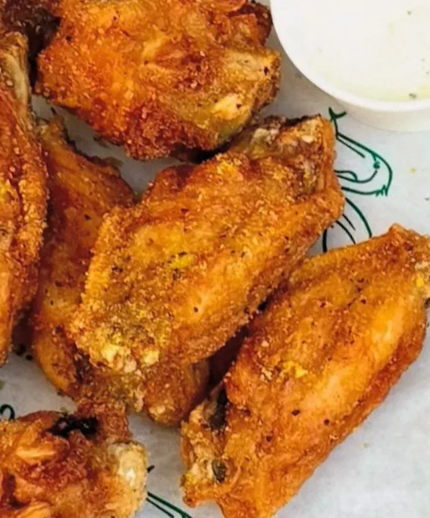 Crispy golden-brown fried chicken wings and a cup of dipping sauce.