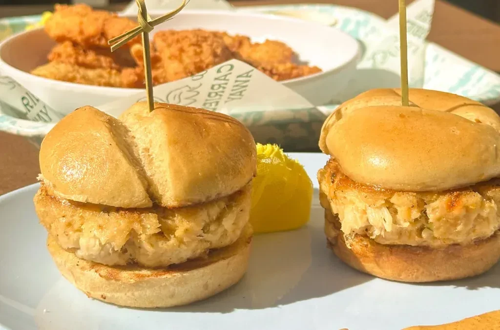 Two crab cake sliders with yellow sauce on a plate.