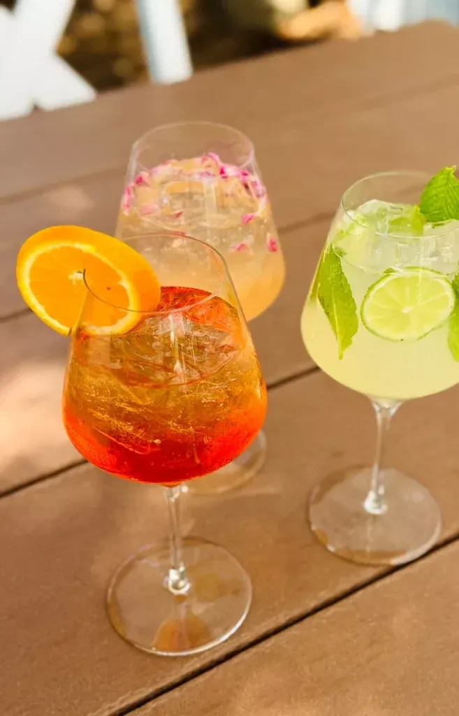 Three colorful garnished cocktails on an outdoor slatted table.