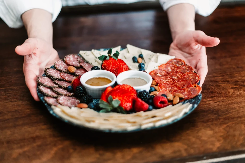 Charcuterie board of meats, cheeses, berries, almonds, and dips, held by hands.