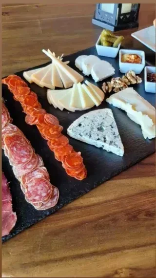 Slate platter with assorted charcuterie, cheeses, pickles, and walnuts.