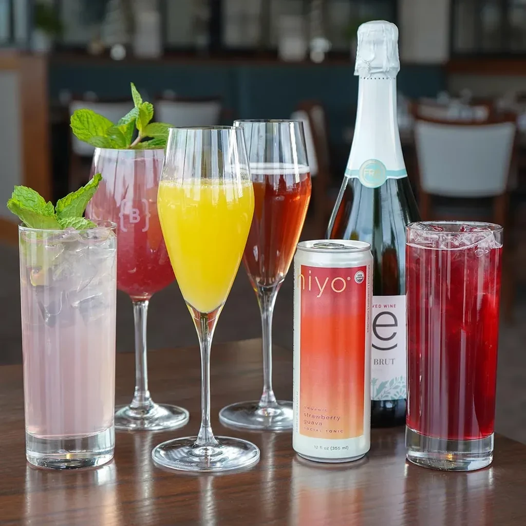 Six colorful drinks, bottle, and can on a polished wooden table.