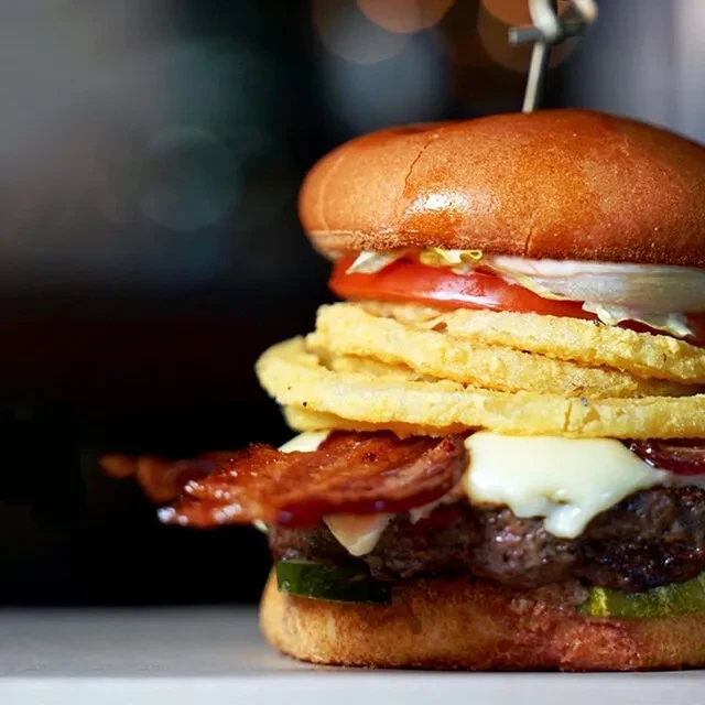 Stacked brioche beef burger with cheese, bacon, onion rings, skewer.