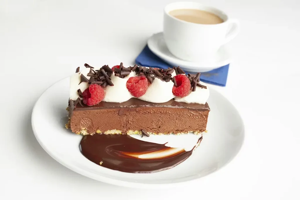 Layered chocolate cake with cream, raspberries, chocolate shavings and sauce.