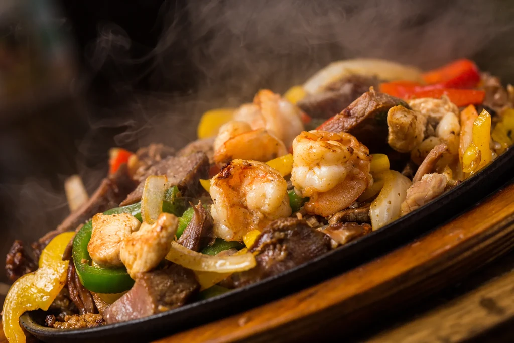 Sizzling beef, chicken, and shrimp fajitas with peppers and onions in a skillet.