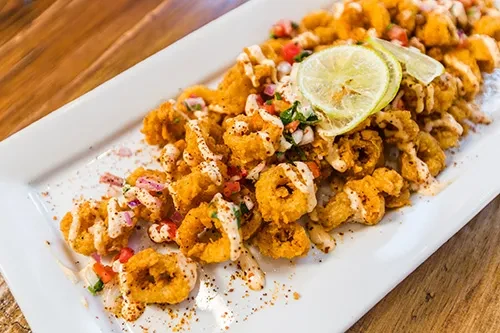 Crispy calamari with pico de gallo, creamy sauce, and lime slices.
