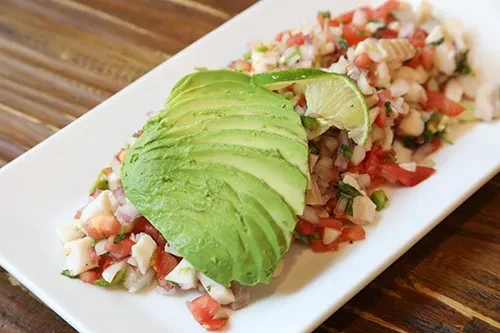 Colorful ceviche with avocado fan and lime on a white plate.