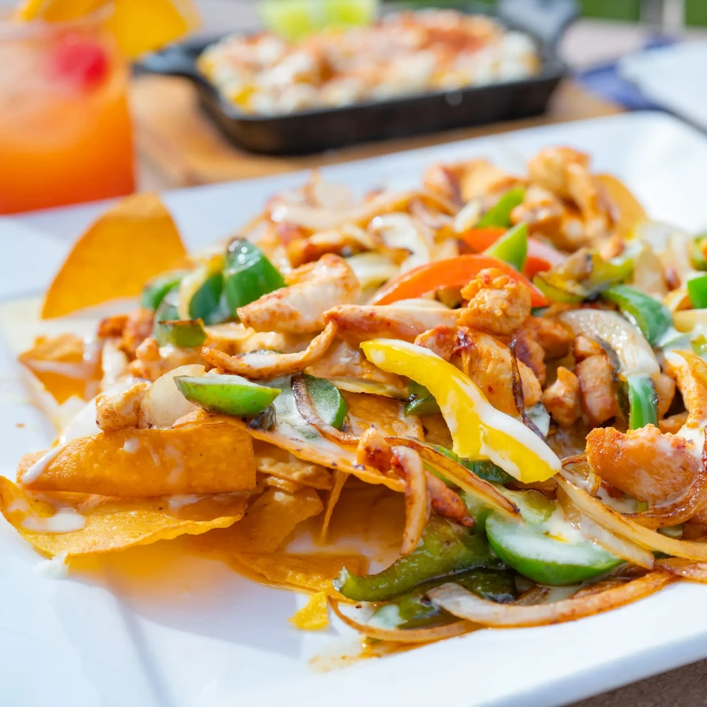 Crispy chicken nachos with colorful peppers, onions, and creamy sauce.