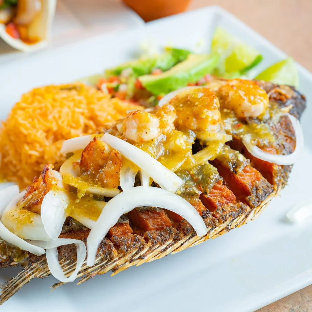 Crispy fried fish topped with green sauce, shrimp, rice, and lime.