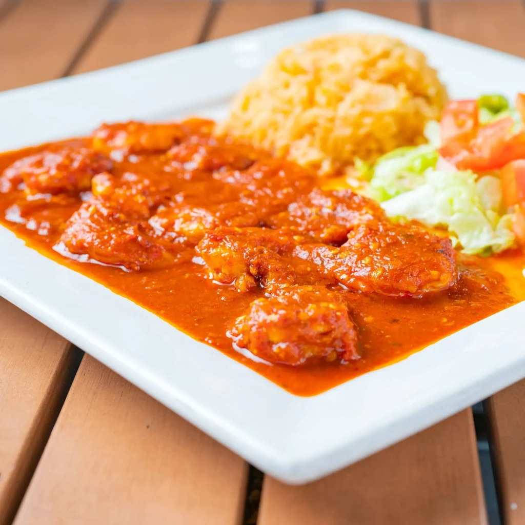 White plate with sauced chicken/shrimp, yellow rice, and salad.