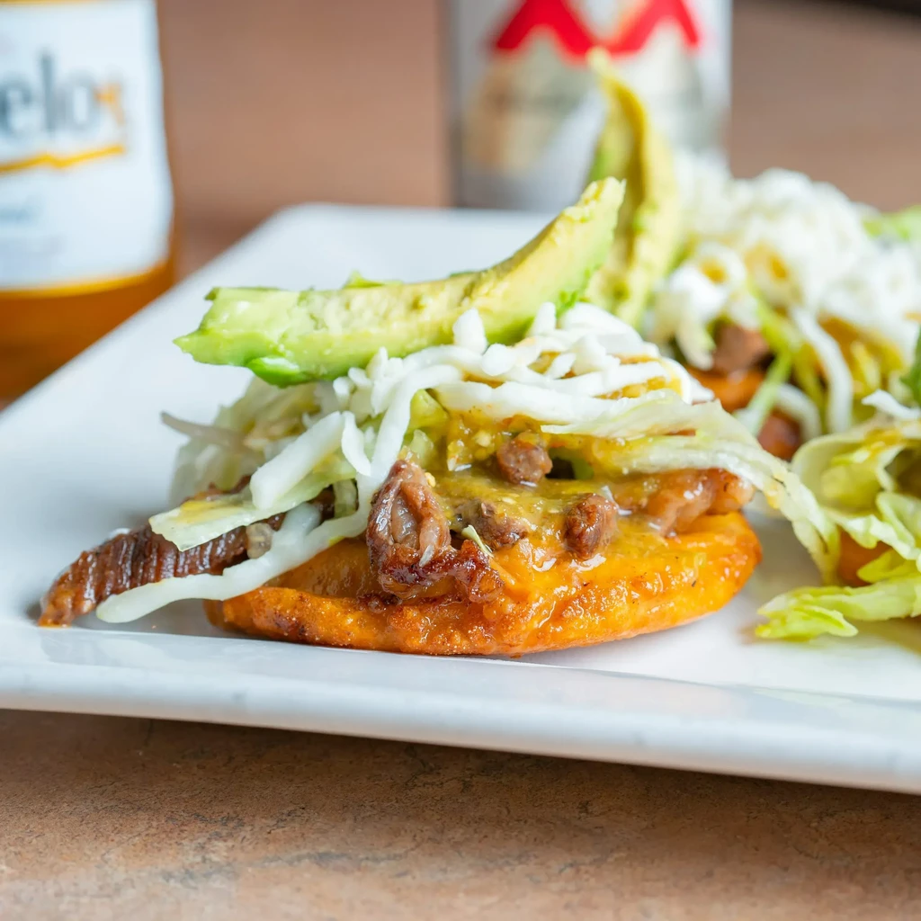 Close-up: Mexican antojito with meat, cheese, green salsa, avocado.