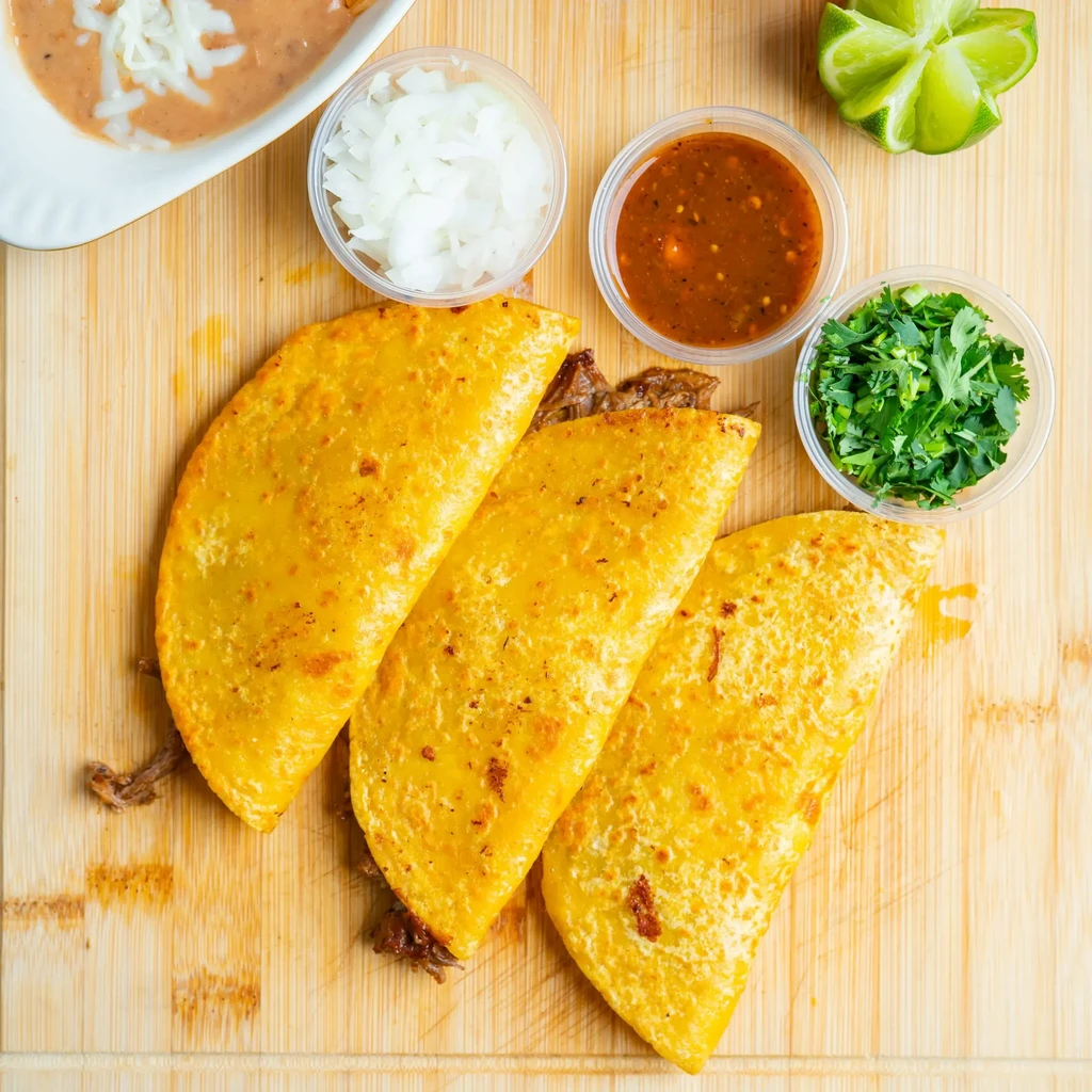 Crispy birria tacos, consommé, cilantro, onions, beans, and lime on board.