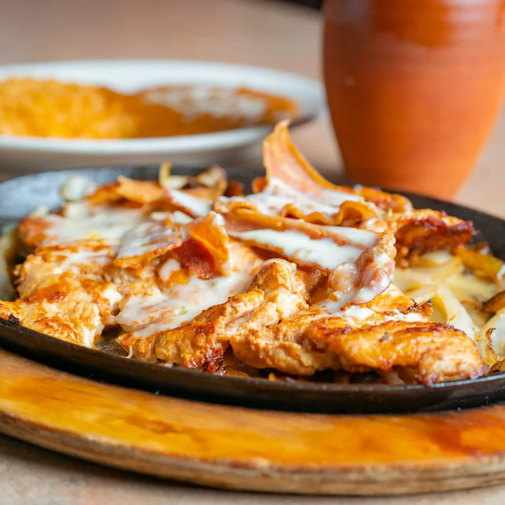 Sizzling chicken or steak with melted cheese and bacon in a skillet.