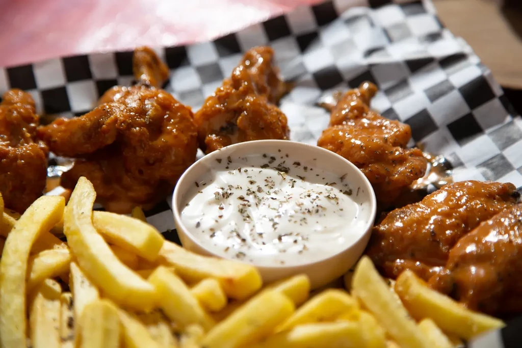 Buffalo chicken wings, golden fries, and creamy dipping sauce on a plate.